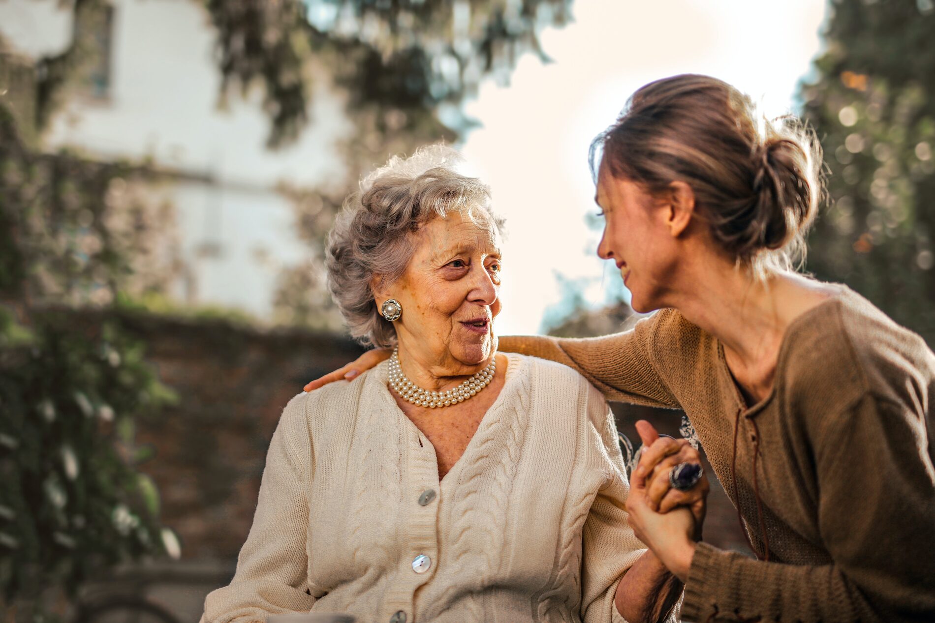 A caregiver and an older woman sharing a warm, candid moment outdoors