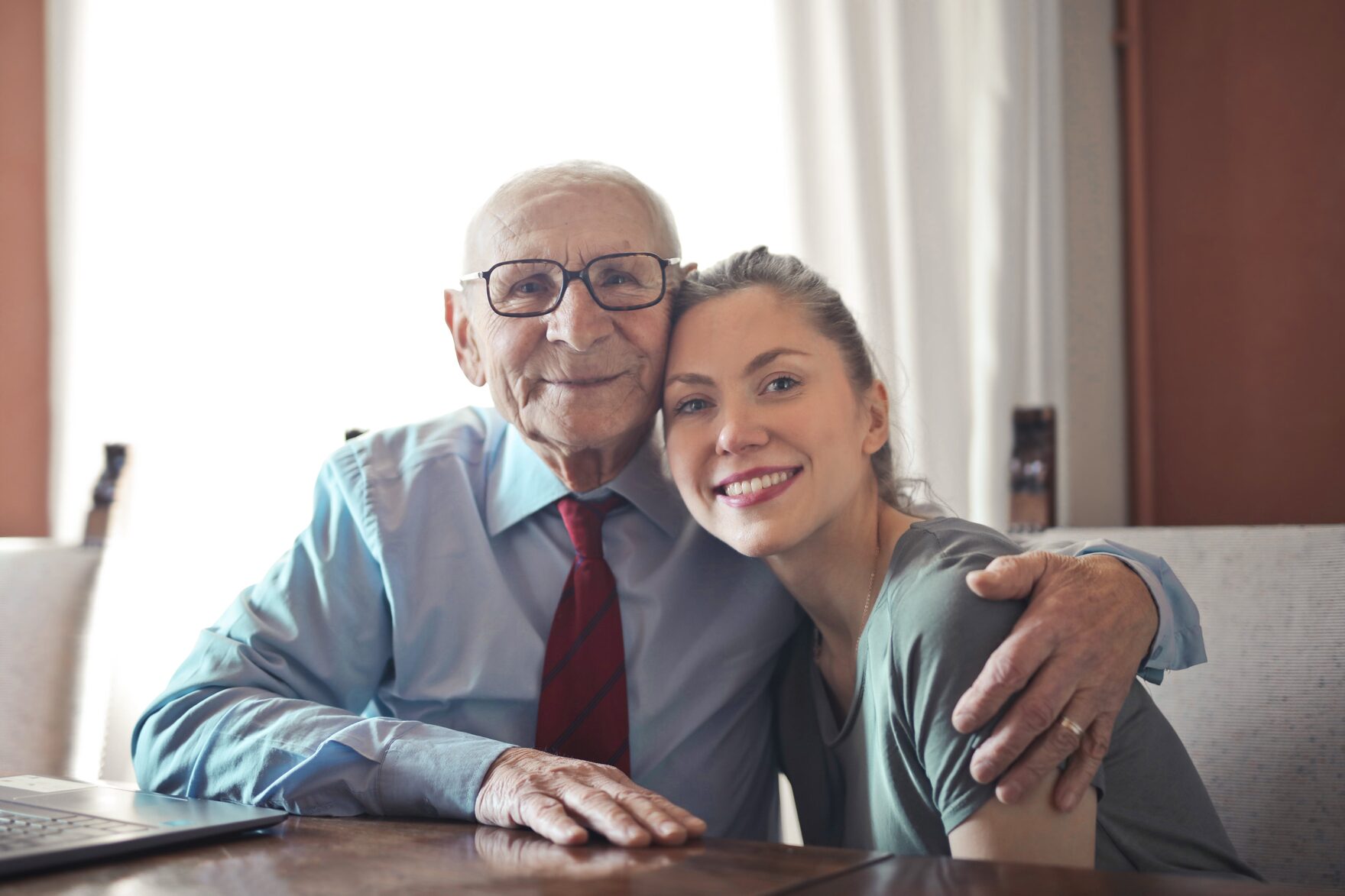 An older man and his adult daughter smiling together at home