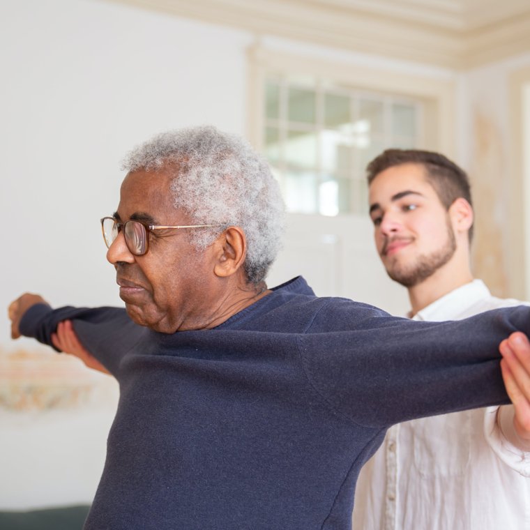 A caregiver helping an older man with mobility exercises