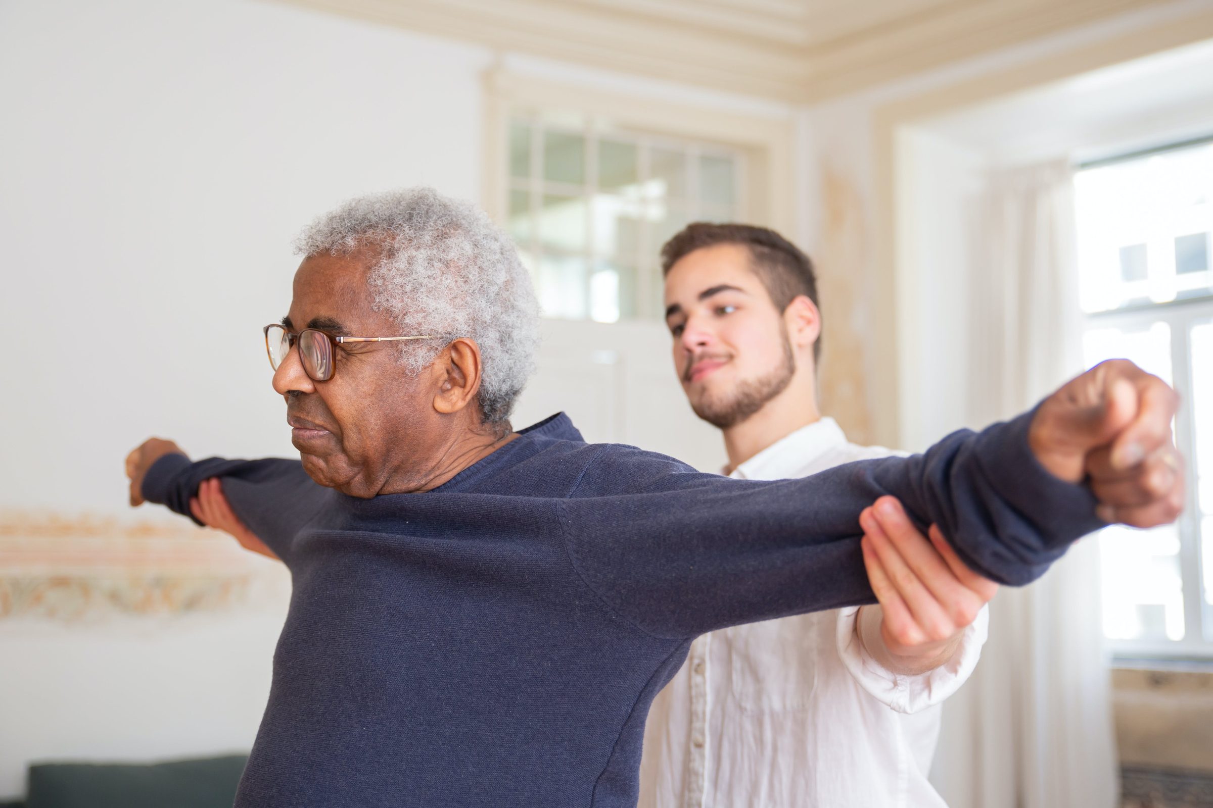 A home caregiver guiding an older man through gentle stretching exercises at home